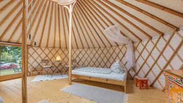 A yurt interior with a bed, seating area, and a view through the entrance.