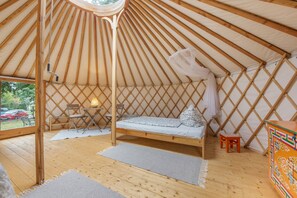 L’intérieur d’une yourte, avec un lit, un coin salon et une vue sur l’extérieur, visible par l’entrée.