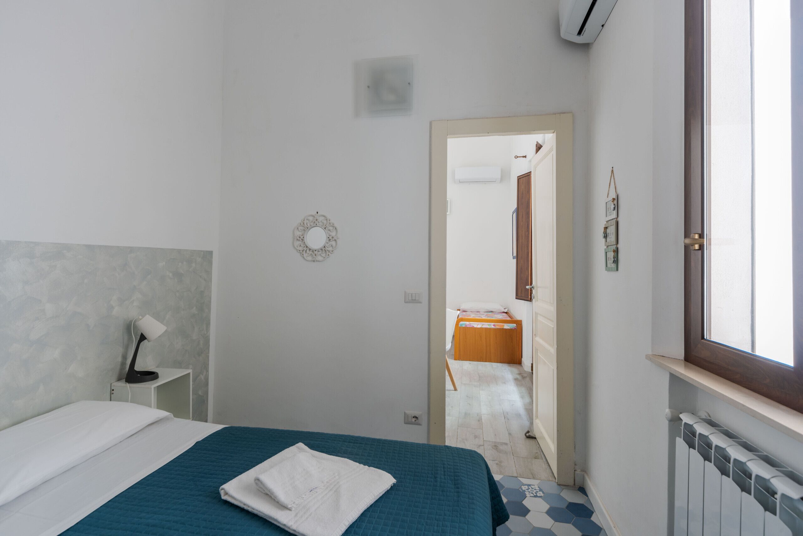 A bedroom with a bed, a bedside table with a lamp, a mirror, and a door leading to a bathroom.