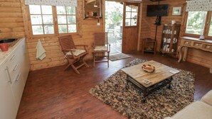 A rustic wooden cabin interior with a dining area, two wooden chairs, a table with a bowl, a cabinet with dishes, and a television. - Carps Well Lodge (Warwick)