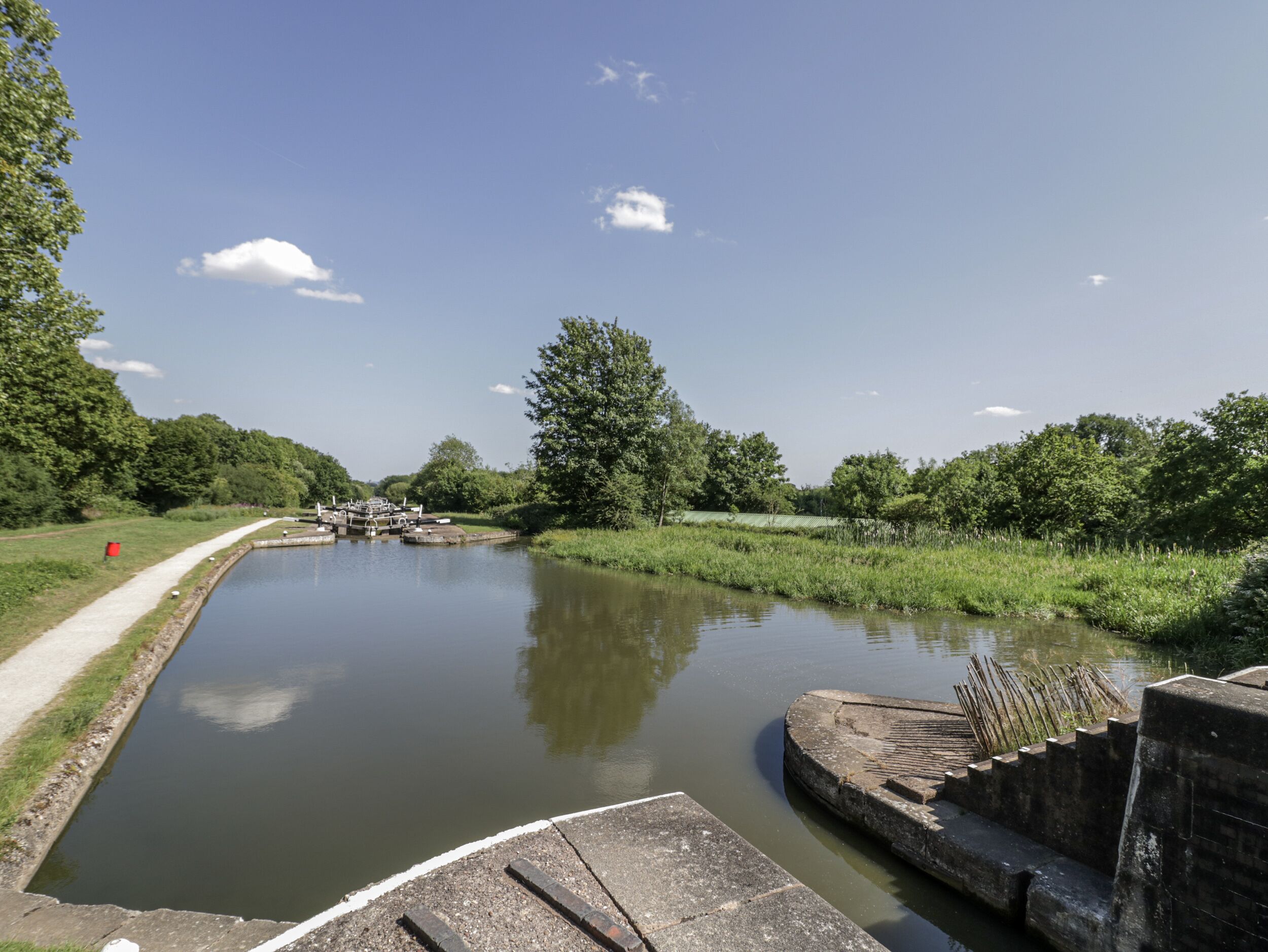 A narrow canal with a lock system, surrounded by greenery and trees.