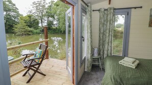 A room with a bed, a chair, a small table, and a view of a river. - Carps Well Lodge (Warwick)