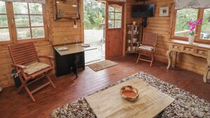 A wooden cabin interior with a dining table, two chairs, a television, and a window with a view of greenery. - Carps Well Lodge (Warwick)