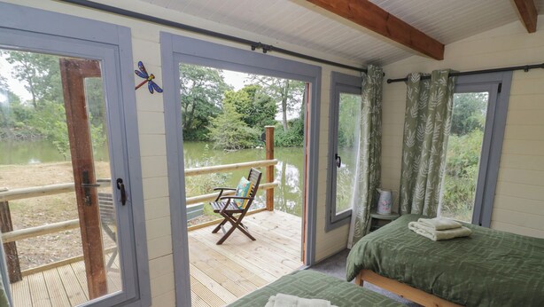 A room with two beds, a wooden deck, a chair, and a view of a lake. - Carps Well Lodge (Warwick)
