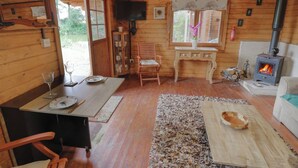 A cozy cabin interior with a dining area, a wooden table, a sofa, a fireplace, and a television. - Carps Well Lodge (Warwick)