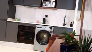 A compact kitchen with a built-in washer and dryer, a microwave, and a small countertop area with potted plants.