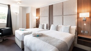 Habitació d'hotel amb dos llits, un escriptori, una cadira i una finestra gran amb cortines.