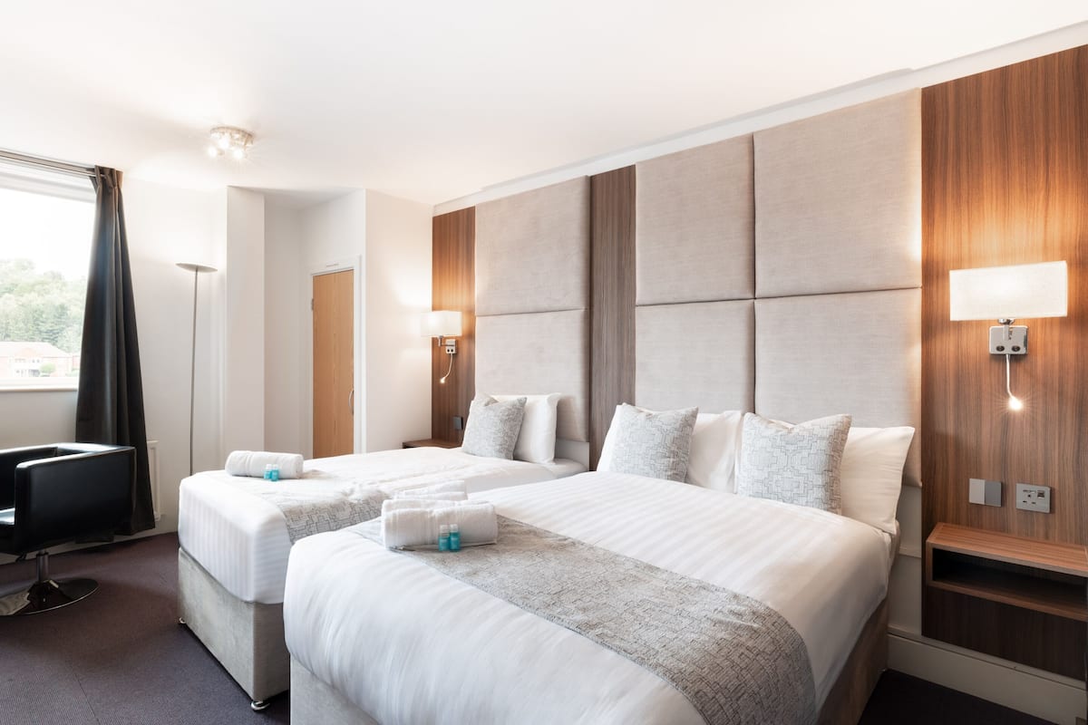 A hotel room with two beds, a desk, a chair, and a large window with curtains.