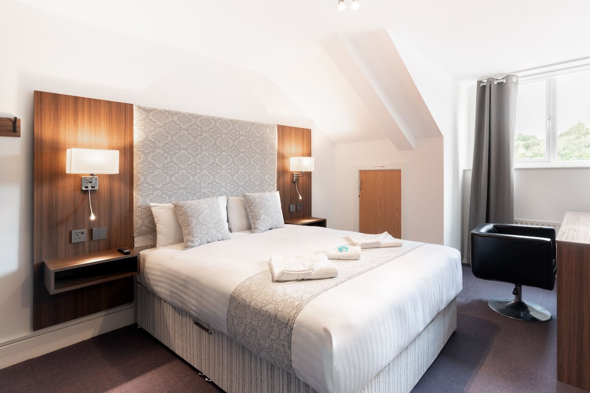 A hotel room with a large bed, two bedside tables, a desk, and a chair.