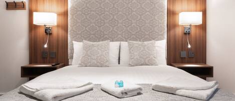 A hotel room with a large bed, two bedside lamps, a wooden headboard, and a small table with a remote control.