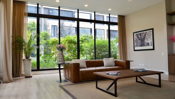 A spacious living room with a leather sofa, a coffee table, and large windows offering a view of greenery outside. - NOK Cozy Studio in Parque Virrey (Bogotá)