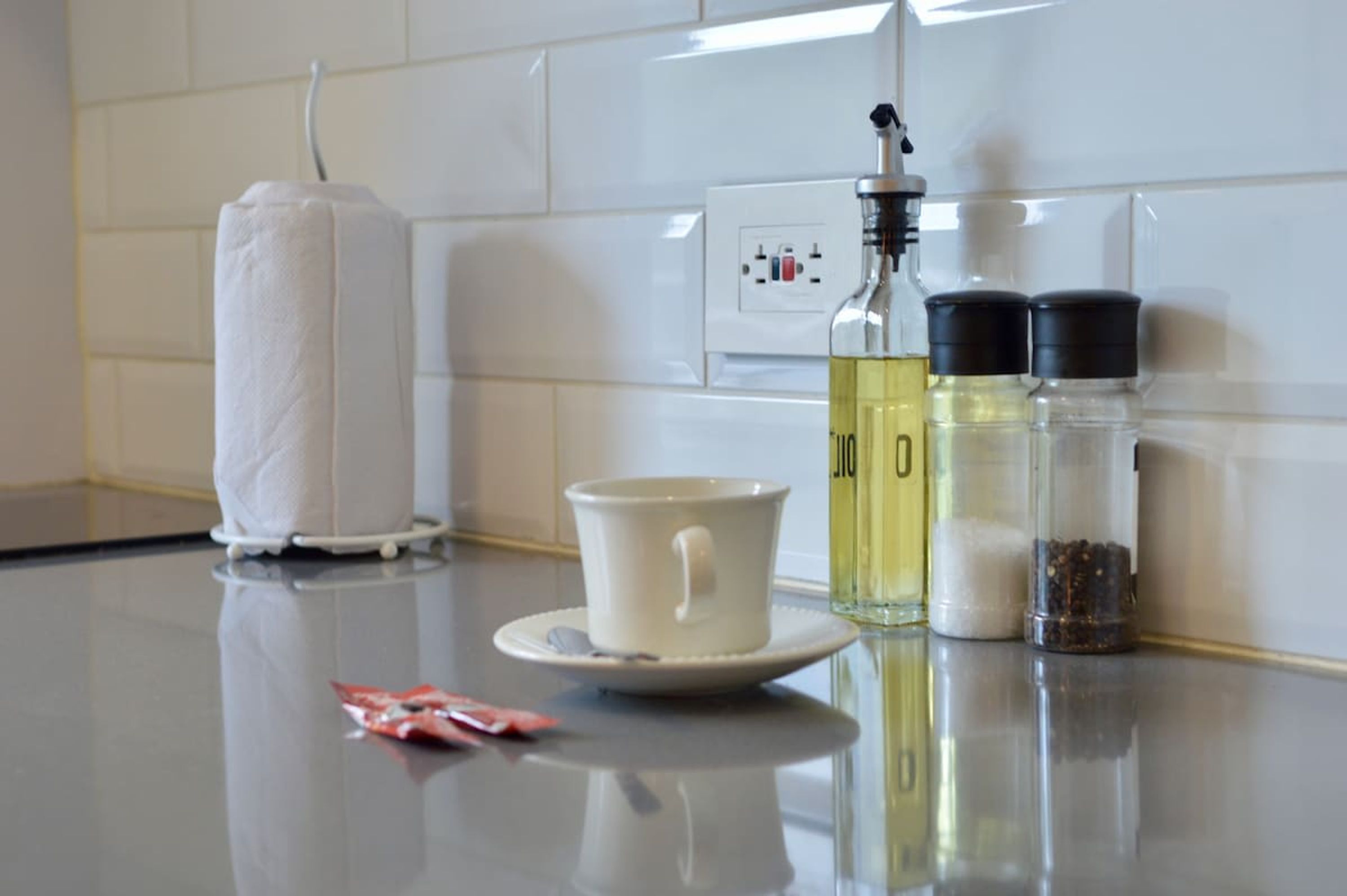 A kitchen counter with a white mug, a bottle of oil, salt and pepper shakers, and a roll of paper towels.