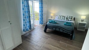 Une chambre à coucher comprenant un lit, une table de chevet, un ventilateur de plafond et une vue sur l’extérieur par une porte.