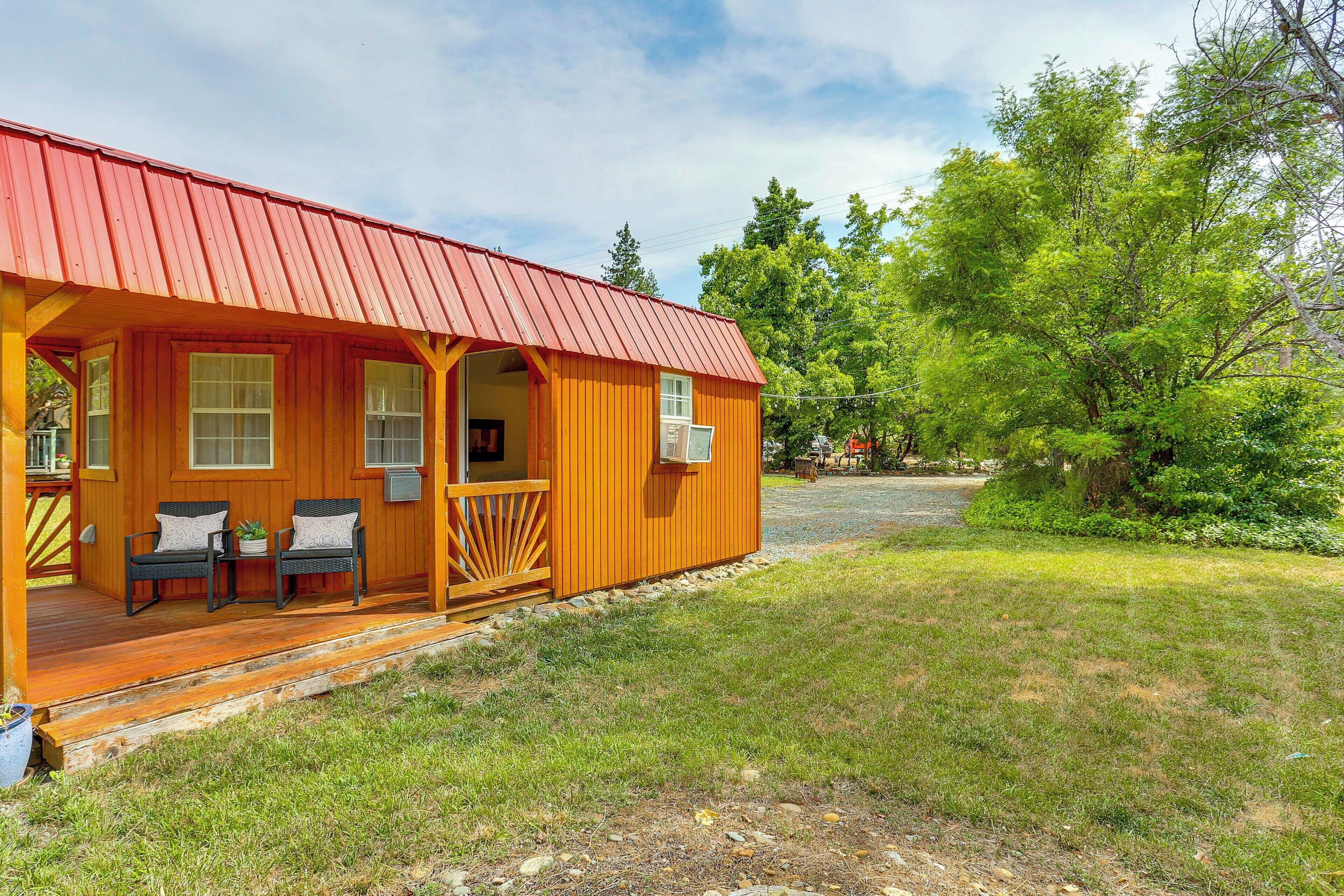 Una cabaña de madera con techo rojo, un porche con dos sillas y una pequeña terraza.