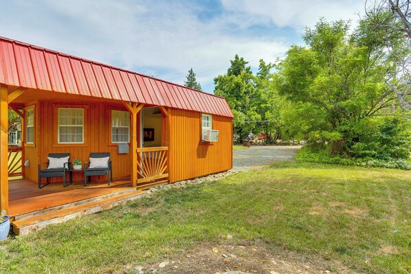 Une cabane en bois avec un toit rouge, une véranda avec deux chaises et une petite terrasse.