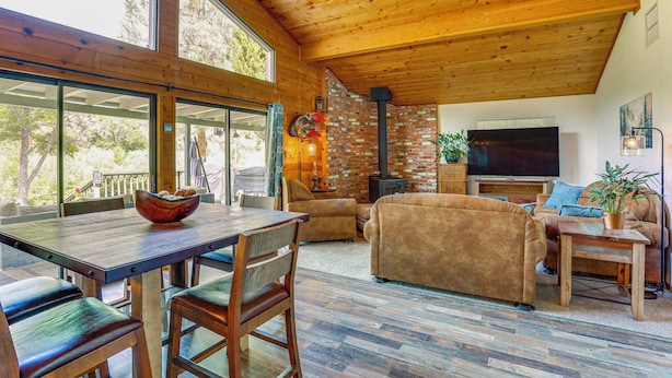 A spacious living area with a wooden ceiling, a brick fireplace, and a large TV. - Scenic Riverfront Escape w/ Sauna in Junction City (Junction City)