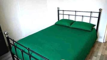 A single bed with a metal frame and green bedding in a room with wooden flooring and white walls.