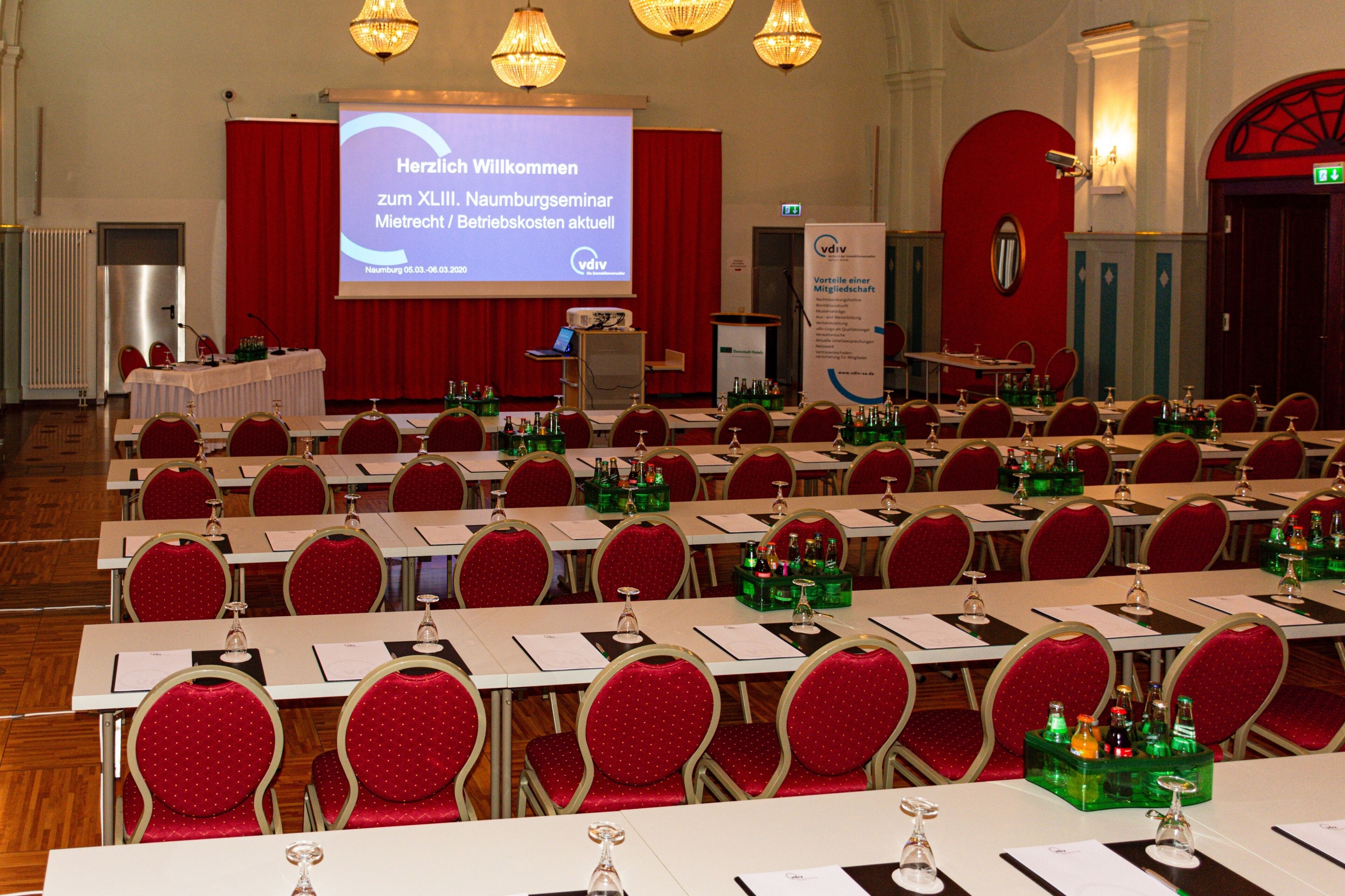 A conference room with rows of tables and chairs, a projection screen, and a podium.