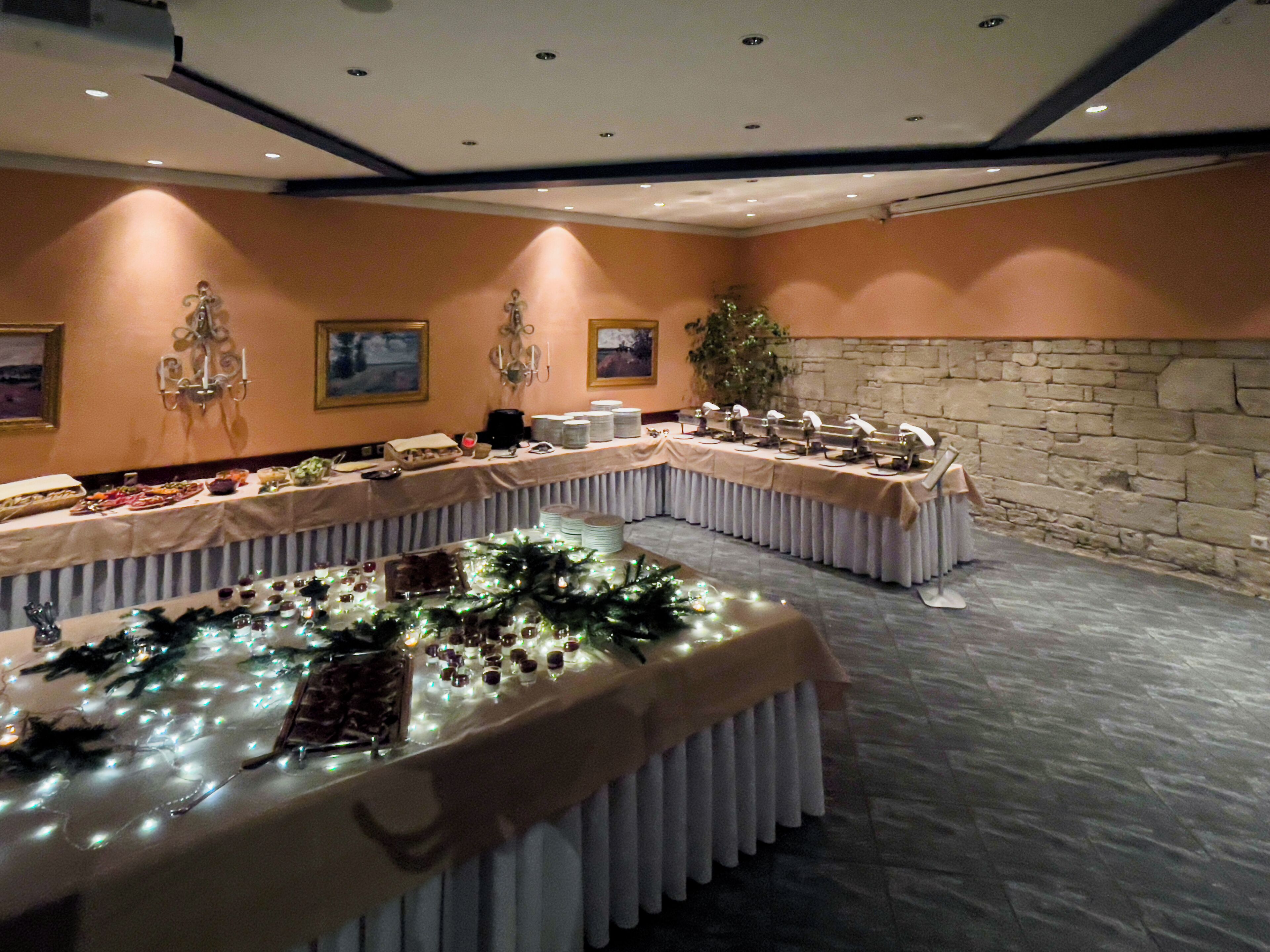 A banquet hall with long tables, a stone wall, and wall-mounted lighting fixtures.