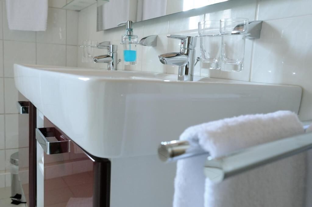 Un baño moderno con un lavamanos blanco, grifos cromados y un perchero para toallas.