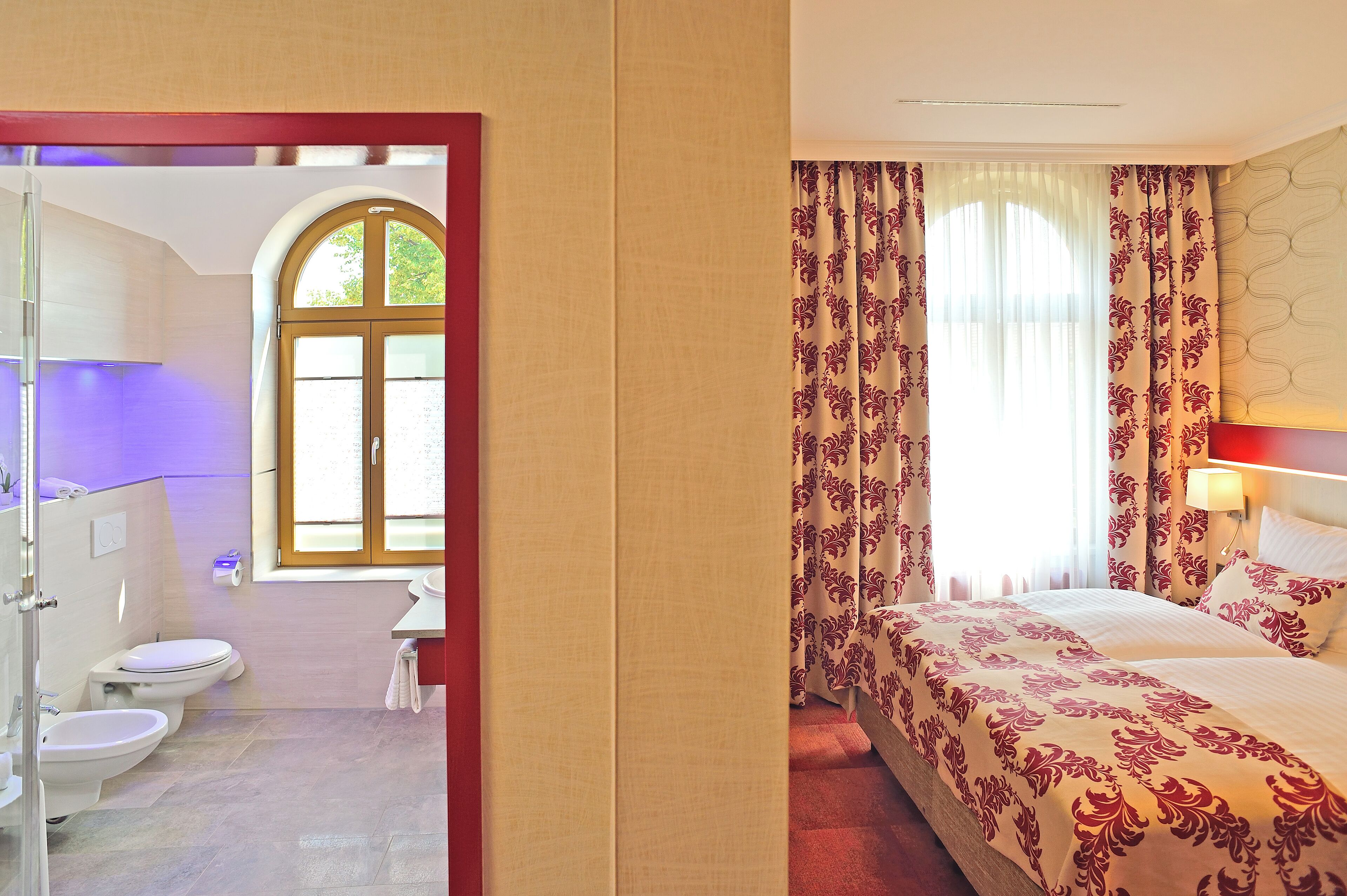 Une chambre d’hôtel avec un lit, une salle de bain comprenant des toilettes et un lavabo, et une fenêtre avec des rideaux.