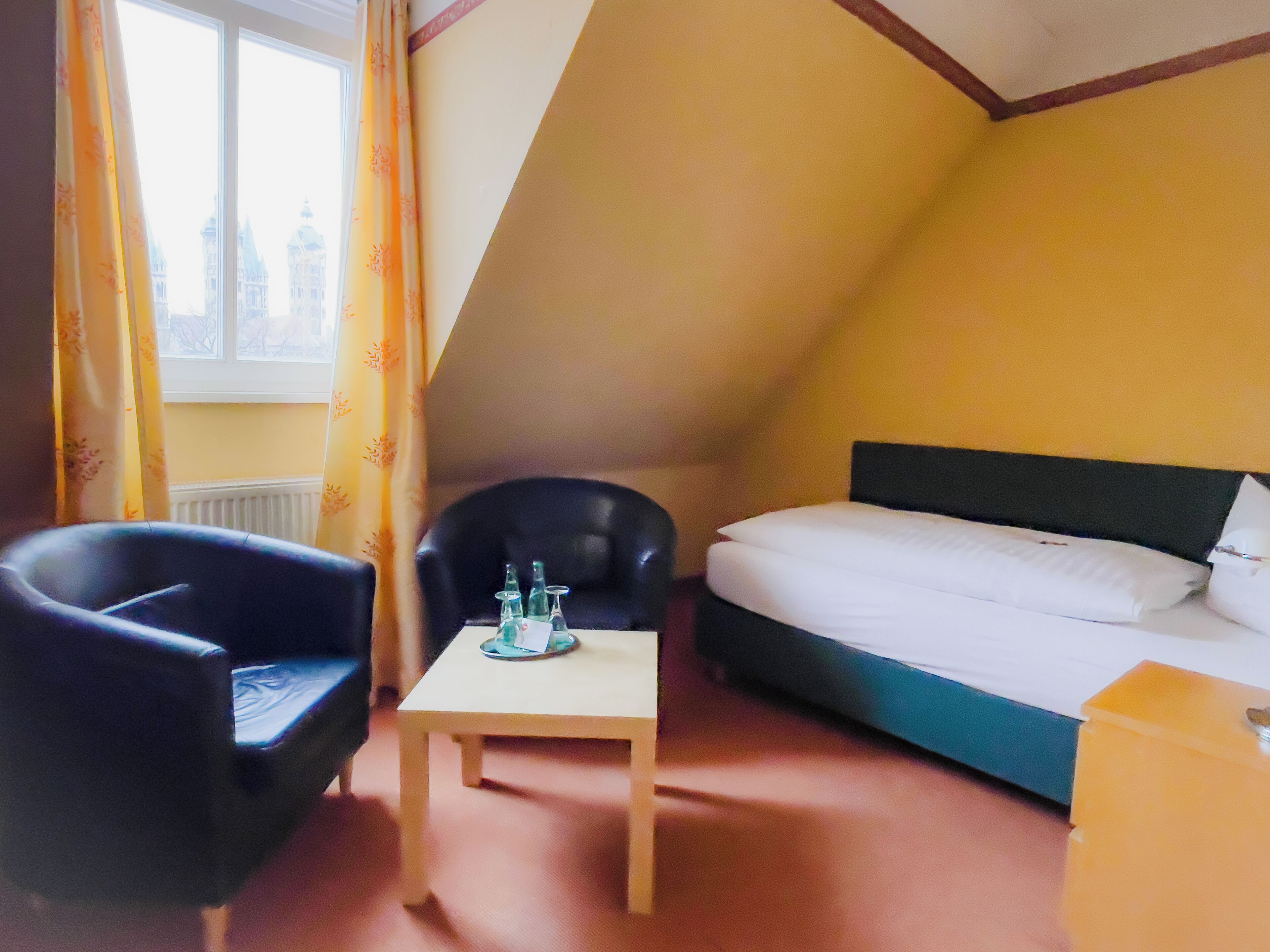 A small, triangular room with a bed, a table, and two chairs.