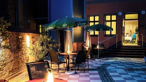 Een terras met tafels en stoelen, een stenen muur en een toegang tot een gebouw.
