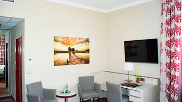 A hotel room with a TV, two chairs, a small table with drinks, and a painting of a sunset over a pier.