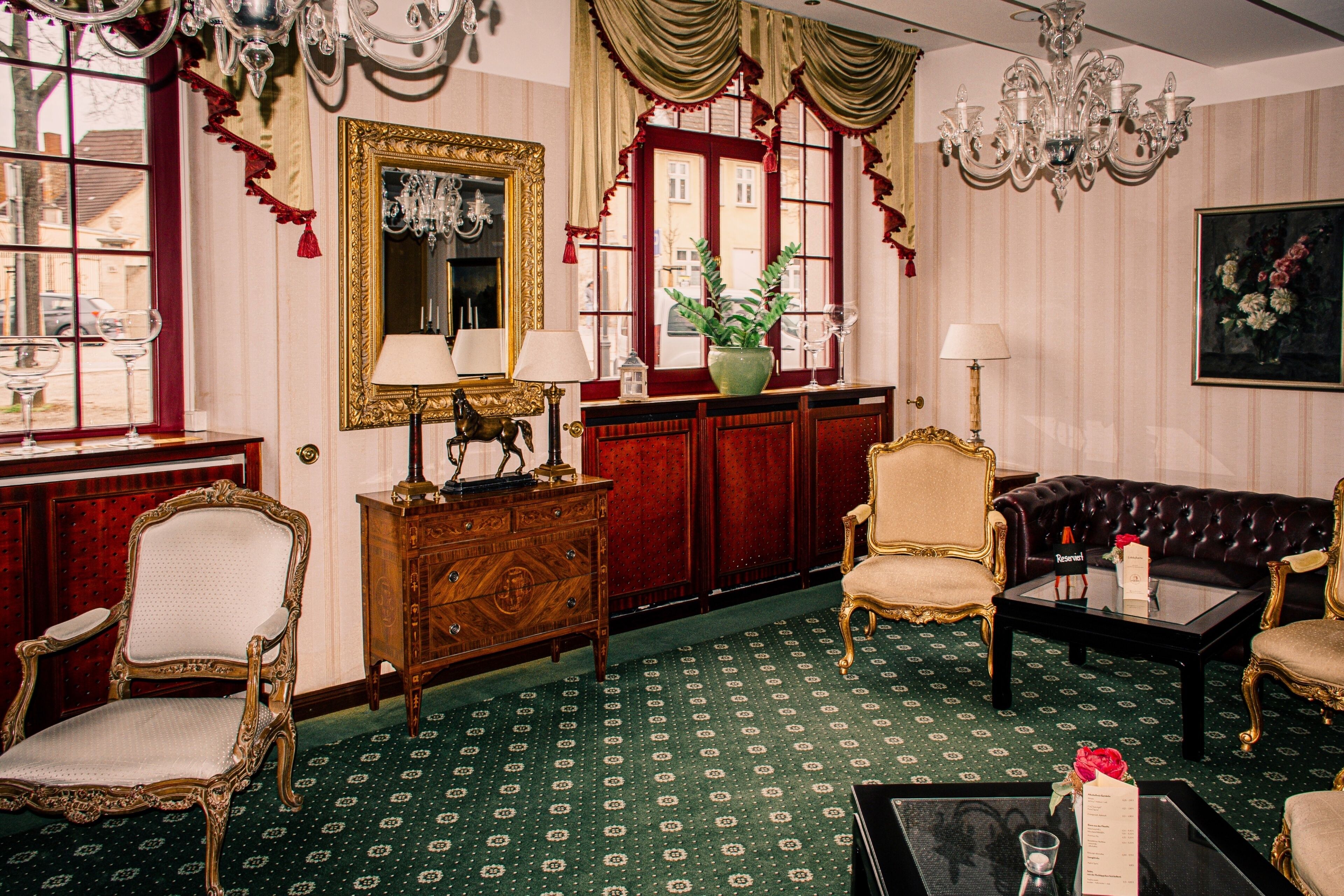 A room with a green patterned carpet, a wooden cabinet, a mirror, a sofa, and a chandelier.
