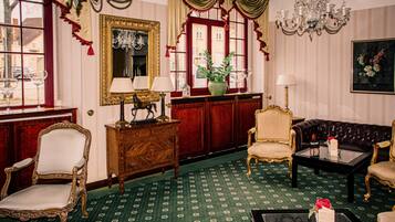A room with a green patterned carpet, a wooden cabinet, a mirror, a sofa, and a chandelier.