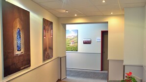 Een hal met houten vloer, een receptiebalie met een potplant en borden met richtingaanwijzingen aan de muur.