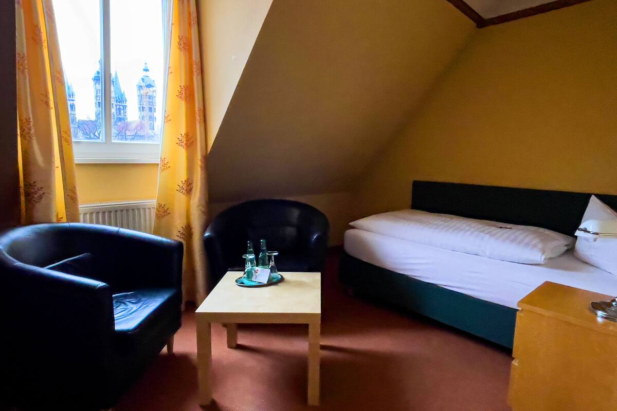 Una habitación con cama, dos sillones, una mesita y una ventana con cortinas.