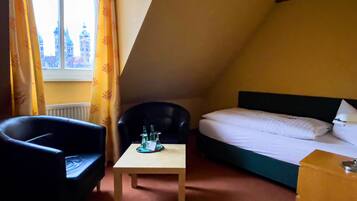 A room with a bed, two chairs, a small table, and a window with curtains.