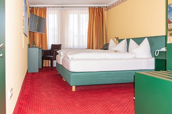 Habitación de hotel con cama, escritorio, televisión y ventana con cortinas.