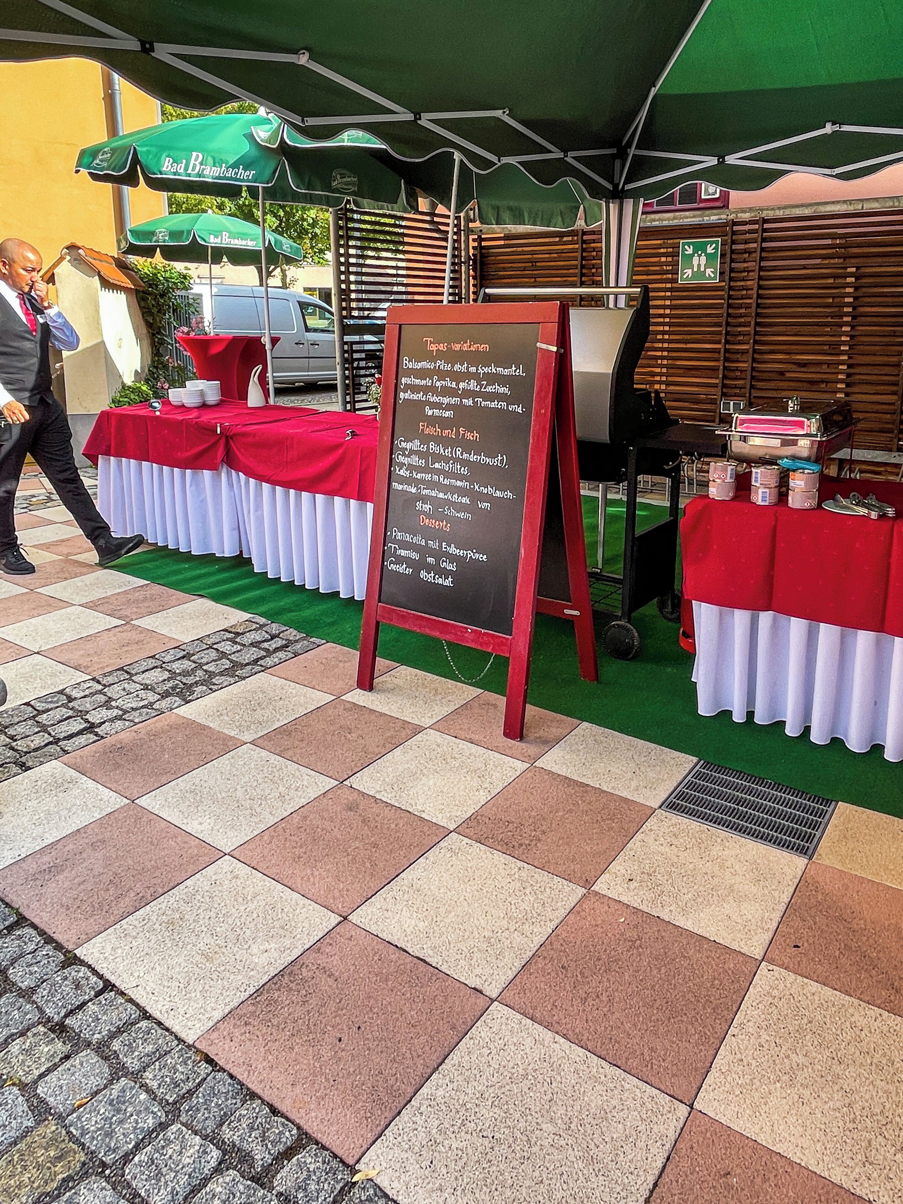 Un tablero de menú con opciones de comida, una mesa con mantel rojo y un paraguas verde.