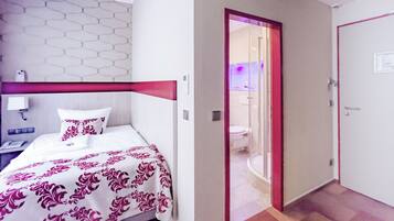 Hotelkamer met een bed, nachtkastje, en een zichtbare badkamer door een geopende deur, plus een rode deur.