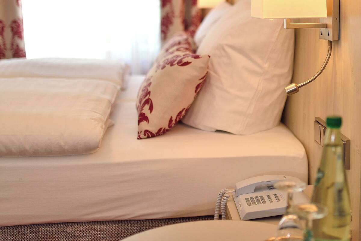 Habitación de hotel con cama, lámpara de noche, teléfono y una botella sobre la mesita de noche.