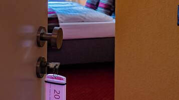 A hotel room with a bed, a red carpet, and a door with a keycard lock.