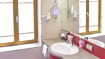 A bathroom with a large window, a round mirror, a sink, and a red vanity.