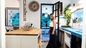 Une cuisine avec un îlot central en bois, un évier et une cuisinière. Il y a une fenêtre donnant sur des arbres et une porte menant à une autre pièce.