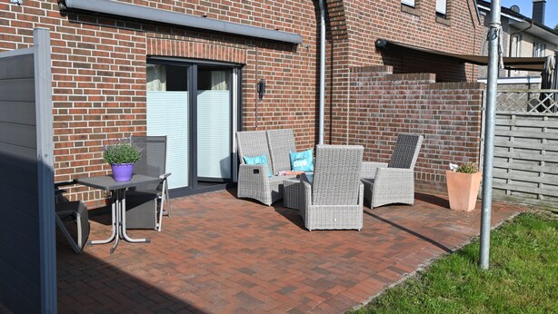 Een terras met rieten meubels en een tafel, een bakstenen gebouw met een garagedeur, en een metalen hek.