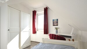Een slaapkamer met een bed, een bureau, een raam met gordijnen en een deur.