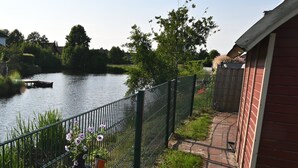 Uitzicht op een rivier met een houten steiger, een metalen hek en een rood gebouw.
