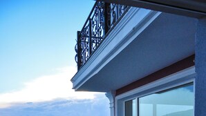 A balcony with wrought iron railings overlooking a cityscape with red-roofed buildings and a clear sky.