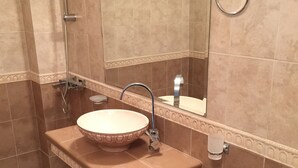 A bathroom with a pedestal sink, a handheld showerhead, a toilet, and a towel ring.