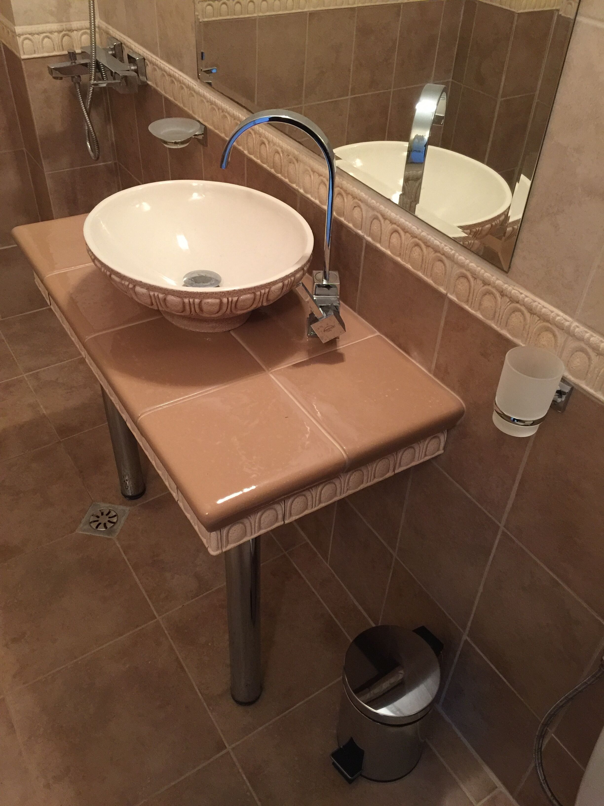 Un baño con un lavamanos color beige, un espejo y un cabezal de ducha manual.