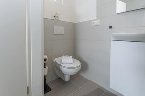 Une petite salle de bain moderne, équipée de toilettes, d’un distributeur de papier toilette fixé au mur et d’une petite plante en pot.