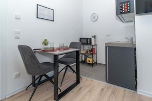 A compact kitchen with a dining table, chairs, a microwave, a small refrigerator, and a sink. - LiT LiVING: Luxus | Box SprIng | Kitchen | Parking (Altenstadt)