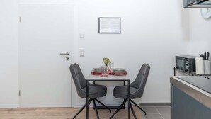 A compact kitchen with a microwave, a small table with two chairs, and a framed document on the wall. - LiT LiVING: Luxus | Box SprIng | Kitchen | Parking (Altenstadt)