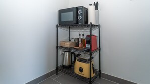 A kitchen area with a black microwave on the top shelf, a yellow toaster on the bottom shelf, and a kettle on the middle shelf. - LiT LiVING: Luxus | Box SprIng | Kitchen | Parking (Altenstadt)